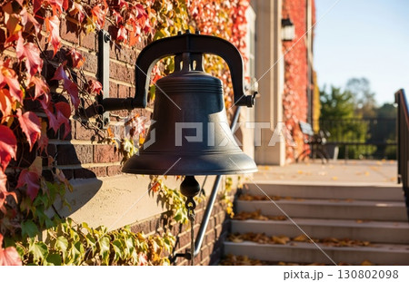 Morning light on school bell wall with red ivy and scattered leaves on steps 130802098