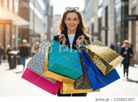 Smiling woman walking with colorful shopping bags in bright urban outdoor environment Smiling woman walking with colorful shopping bags in bright urban outdoor environment 130802307