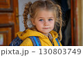 Little girl with braids in yellow jacket and backpack standing by the doorway 130803749