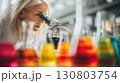 Scientist examining samples through microscope surrounded by colorful lab glassware 130803754