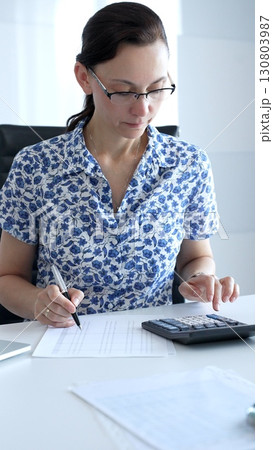 Businesswoman using calculator and filling tax form, calculating expenses and managing financial data in office. Audit and taxes in business 130803987