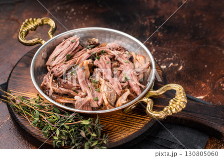 Close-up of succulent pulled brisket piled high on a rustic wooden board, garnished with fresh herbs, delicious meal. brown background. top view 130805060