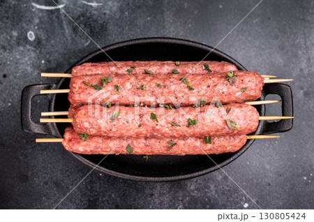 Raw shish kebab, arabic kofta kofte kebab from mince lamb and beef meat on Skewer. black background. top view Raw shish kebab, arabic kofta kofte kebab from mince lamb and beef meat on Skewer. black background. top view 130805424