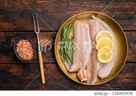 Pollock sea fish fillets, raw whitefish on a plate with herbs and lemon. wooden background. top view Pollock sea fish fillets, raw whitefish on a plate with herbs and lemon. wooden background. top view 130805476