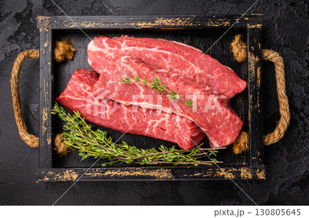 Raw skirt or machete Steak, beef meat in wooden tray with herbs. black background. top view Raw skirt or machete Steak, beef meat in wooden tray with herbs. black background. top view 130805645