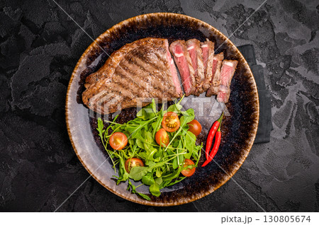 Grilled striploin steak, beef meat steak on a plate with salad. black background. top view Grilled striploin steak, beef meat steak on a plate with salad. black background. top view 130805674