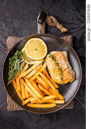 Homemade Fish and chips with roast cod whitefish fillet and fried potatoes on plate. black background. top view 130805686