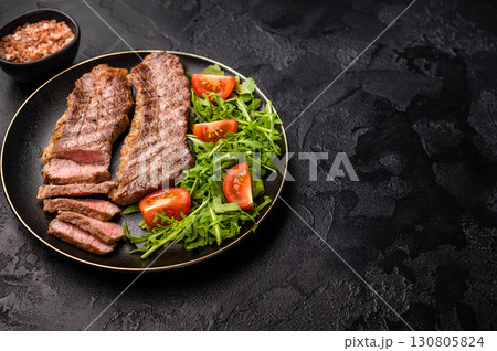 Grilled Steak from Black Angus beef meat on a plate with salad. black background. top view 130805824