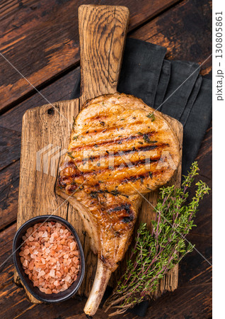 Tender grilled Tomahawk pork chop, showcasing its rich marbling and smoky aroma for a delightful dining experience. wooden background. top view 130805861