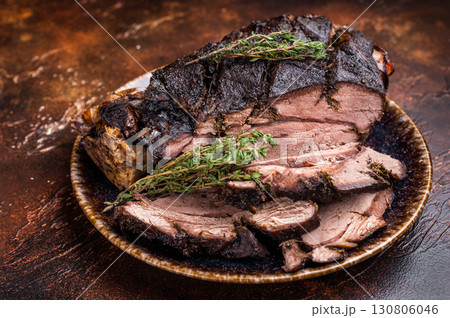 Baked and sliced Venison leg. roast meat of deer with bone on a plate. brown background. top view 130806046