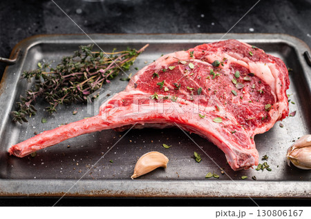 Ready for cooking Tomahawk beef steak with seasonings, raw marbled rib eye with bone on steel tray. black background. top view 130806167