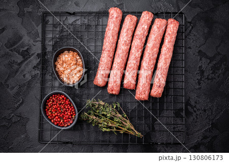 Uncooked Raw Cevapcici Sausage, fresh Cevapi from mince beef and pork meat on a rack. black background. top view 130806173