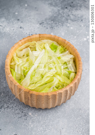 Fresh raw iceberg lettuce salad cut leaves in wooden bowl. grey background. top view 130806301