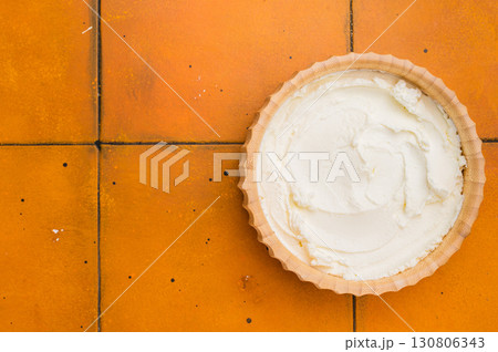 Cream texture, Mascarpone Italian cream cheese in wooden bowl. orange background. top view Cream texture, Mascarpone Italian cream cheese in wooden bowl. orange background. top view 130806343