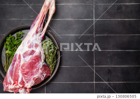 Uncooked whole lamb leg, raw mutton meat with herbs for cooking. black background. top view Uncooked whole lamb leg, raw mutton meat with herbs for cooking. black background. top view 130806505