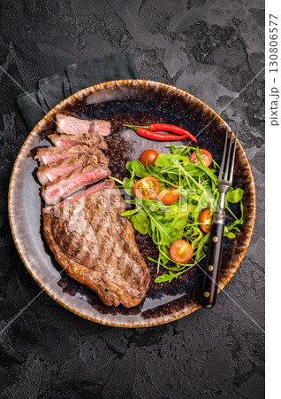Grilled striploin steak, beef meat steak on a plate with salad. black background. top view Grilled striploin steak, beef meat steak on a plate with salad. black background. top view 130806577