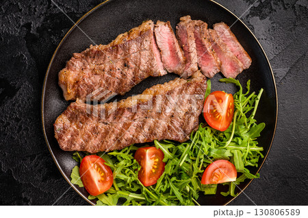 Grilled Steak from Black Angus beef meat on a plate with salad. black background. top view 130806589