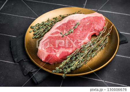 Raw Striploin steak, New York strip beef steak in a plate with herbs. black background. top view 130806676