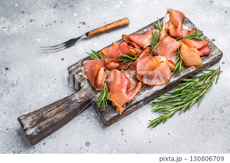 Italian Prosciutto ham, Parma ham on wooden board with rosemary. grey background. top view Italian Prosciutto ham, Parma ham on wooden board with rosemary. grey background. top view 130806709