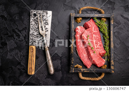 Raw skirt or machete Steak, beef meat in wooden tray with herbs. black background. top view 130806747