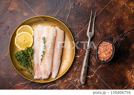 Raw cod loin pieces, whitefish fillets without skin on plate with herbs. brown background. top view Raw cod loin pieces, whitefish fillets without skin on plate with herbs. brown background. top view 130806756