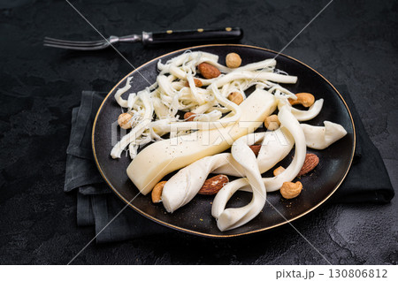 Smoked Traditional Chechil white cheese on a plate with nuts, black background. Smoked Traditional Chechil white cheese on a plate with nuts, black background. 130806812