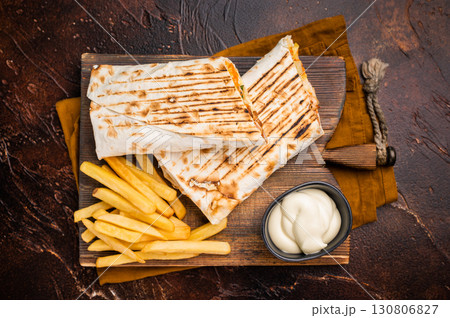 Shawarma chicken roll with fresh vegetables, cream sauce and french fries on wooden board. brown background. top view 130806827