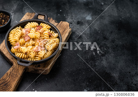 Fusilli carbonara pasta topped with crispy bacon bits and parmesan cheese in a skillet. Black background. Top view Fusilli carbonara pasta topped with crispy bacon bits and parmesan cheese in a skillet. Black background. Top view 130806836
