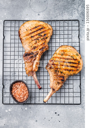 Juicy grilled pork Tomahawk chop, perfectly seared and bursting with flavor, ideal for a hearty feast. grey background. top view Juicy grilled pork Tomahawk chop, perfectly seared and bursting with flavor, ideal for a hearty feast. grey background. top view 130806895