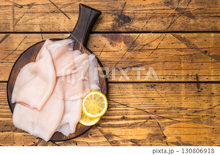 Freshly caught raw squid with glistening skin, perfect for grilling or frying to create mouthwatering dishes. wooden background. top view Freshly caught raw squid with glistening skin, perfect for grilling or frying to create mouthwatering dishes. wooden background. top view 130806918