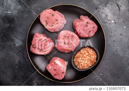 Tender fresh pork medallion, raw tenderloin meat perfect for elevating your dinner table with a touch of culinary finesse. black background. top view Tender fresh pork medallion, raw tenderloin meat perfect for elevating your dinner table with a touch of culinary finesse. black background. top view 130807073