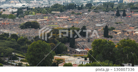 Aerial view of the ancient ruins of Pompeii in Italy, featuring the amphitheater, city layout, dense greenery, and modern urban areas in the distance. Aerial view of the ancient ruins of Pompeii in Italy, featuring the amphitheater, city layout, dense greenery, and modern urban areas in the distance. 130807336