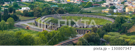 Aerial view of the oval shaped Roman amphitheater in Pompeii, Italy, surrounded by greenery, open spaces, and modern residential buildings. Aerial view of the oval shaped Roman amphitheater in Pompeii, Italy, surrounded by greenery, open spaces, and modern residential buildings. 130807347
