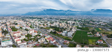 Aerial perspective of Pompei, Italy, showing urban buildings, roads, railways, green fields, and mountains under a cloudy sky in the background. Aerial perspective of Pompei, Italy, showing urban buildings, roads, railways, green fields, and mountains under a cloudy sky in the background. 130807373