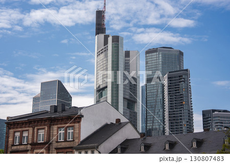 Frankfurt's skyline features the Commerzbank Tower and glass skyscrapers, contrasted by traditional European buildings under a partly cloudy sky. Frankfurt's skyline features the Commerzbank Tower and glass skyscrapers, contrasted by traditional European buildings under a partly cloudy sky. 130807483