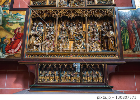 Intricately carved altarpiece in a Frankfurt church, featuring saints, angels, Gothic arches, and painted biblical panels against a red brick wall. Intricately carved altarpiece in a Frankfurt church, featuring saints, angels, Gothic arches, and painted biblical panels against a red brick wall. 130807573