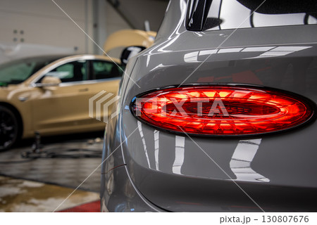 Rear tail light of a Bentley Bentayga with oval red design, parked indoors. A beige luxury car with an open hood is visible in the background. Rear tail light of a Bentley Bentayga with oval red design, parked indoors. A beige luxury car with an open hood is visible in the background. 130807676