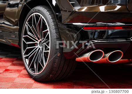 Rear section of a glossy black luxury supercar featuring alloy wheel, low profile tire, quad exhaust pipes, and red checkered flooring in a showroom. Rear section of a glossy black luxury supercar featuring alloy wheel, low profile tire, quad exhaust pipes, and red checkered flooring in a showroom. 130807700