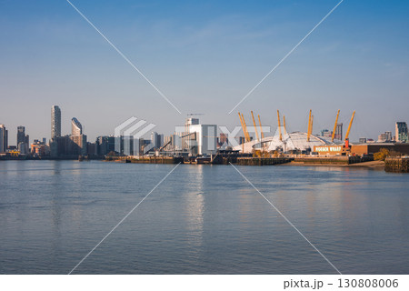 The O2 Arena's white dome and yellow masts stand out along the River Thames, surrounded by modern buildings. The Monier Wharf sign is visible under a clear sky. 130808006
