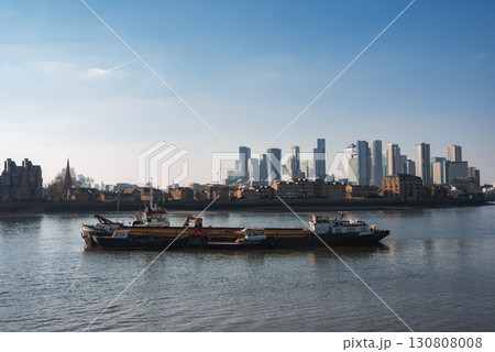 The River Thames features a barge and boats in the foreground, with Canary Wharf's skyscrapers and a church spire contrasting historic and modern London. The River Thames features a barge and boats in the foreground, with Canary Wharf's skyscrapers and a church spire contrasting historic and modern London. 130808008