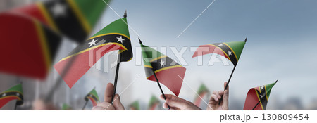 Saint Kitts and Nevis flags in their hands on a blurred urban background Saint Kitts and Nevis flags in their hands on a blurred urban background 130809454