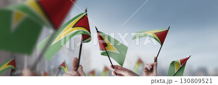 Guyana flags in their hands on a blurred urban background Guyana flags in their hands on a blurred urban background 130809521