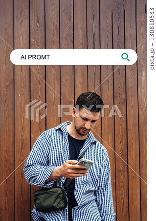 Man checking his phone while standing against a wooden wall in an urban setting during the daytime 130810533