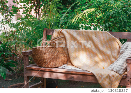Wooden garden bench with yellow blanket and straw basket, place fo relax in cozy summer backyard 130810827
