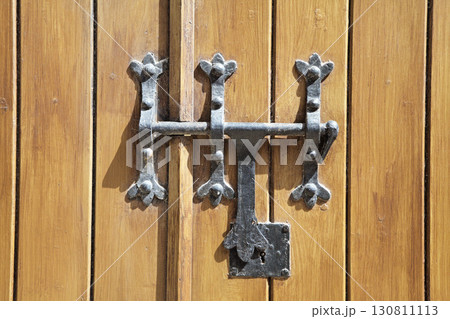 Decorative latch and wooden door with metal hardware in sunlight Decorative latch and wooden door with metal hardware in sunlight 130811113