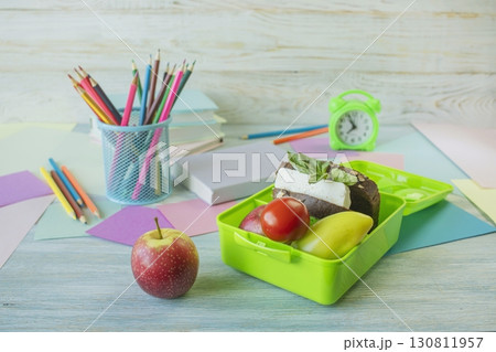 Back to school concept, school food. Lunch box with healthy sandwich, alarm clock, stack of books and  apple on wooden background. 130811957
