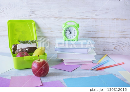 Back to school concept, school food. Lunch box with healthy sandwich, alarm clock, stack of books and  apple on white wooden background. 130812016