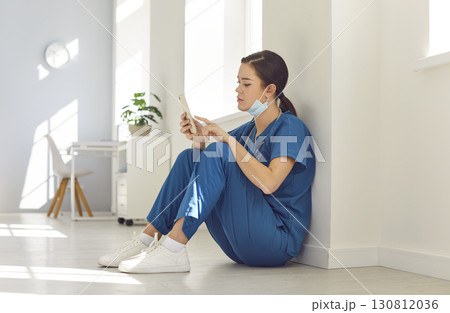 Young female nurse is having a break, sitting on floor and using her mobile phone Young female nurse is having a break, sitting on floor and using her mobile phone 130812036
