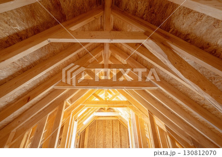 Attic interior of an off-frame construction house with wooden beams and a gable roof structure. Newly constructed A-frame wood attic with beams and unfinished walls. Newly-built buildings, or homes. Attic interior of an off-frame construction house with wooden beams and a gable roof structure. Newly constructed A-frame wood attic with beams and unfinished walls. Newly-built buildings, or homes. 130812070