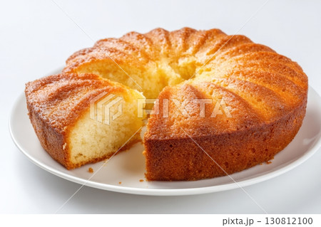 Bundt cake with a crimped top and a glossy sheen on a white plate on a white background. One piece is cut out with soft smooth texture inside. Golden-brown round classic cake and one slice cut out 130812100
